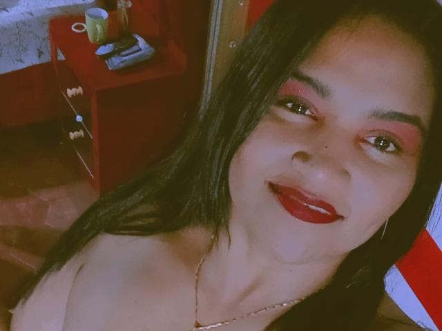 SusanaDiaz has long black hair, red lipstick, and is smiling at the camera. She's wearing a necklace and has visible cleavage. Her makeup includes pink eyeshadow.