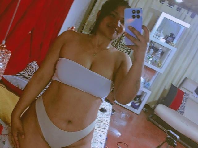 SusanaDiaz with tan skin, black hair, wearing a white strapless bandeau and white panties, holding a blue phone, showing her tits and pussy in a mirror selfie.