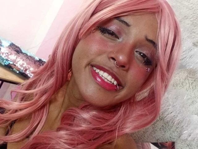LunaKeller with pink hair, nose ring, lip ring, pink glitter eyeshadow, shiny pink lipstick, smiling, winking, long pink wavy hair, cute, sexy, soft light, fluffy white background.