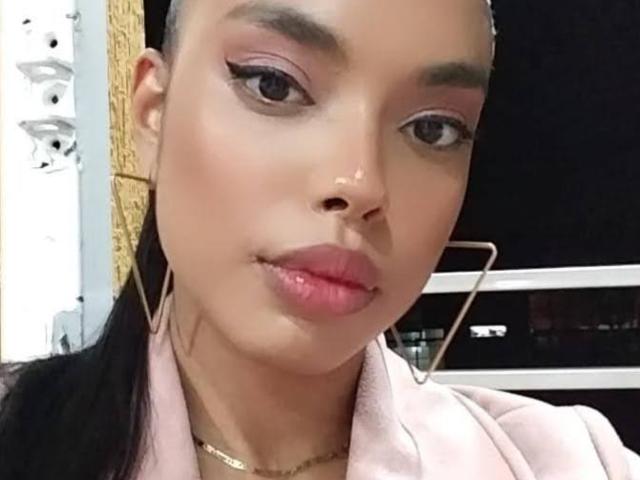EloiseFit has a light brown skin tone, pink eyeshadow, black eyeliner, and pink lipstick. She's wearing a pink jacket, gold necklace, and large geometric earrings.