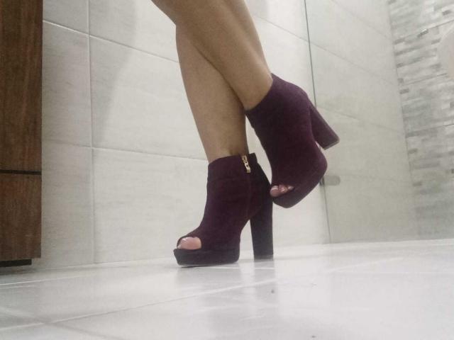 AngeleRoux's legs in dark purple, open-toe, high-heeled boots with a chunky heel, standing on a shiny, white-tiled floor, showing her toes and ankle.