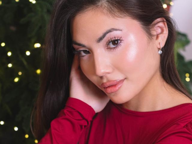 MonicaLuxe has glossy pink lips, shiny skin, brown eyes, and long dark hair, wearing a red shirt, touching her face, with diamond earrings, looking cute and sexy.