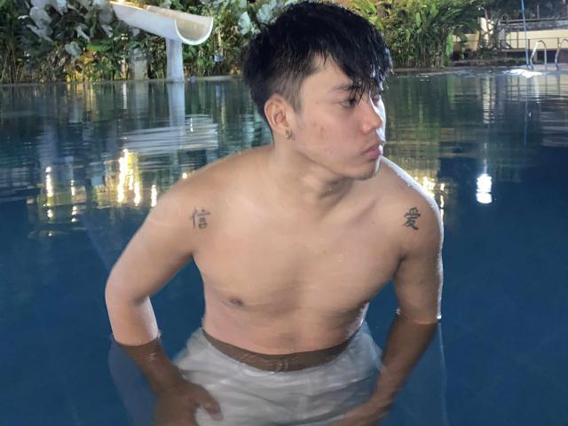 Rayzen69 is in a pool, shirtless, with water up to his waist. He has tattoos on both shoulders, dark wet hair, and a slight beard. His ass is partially submerged.