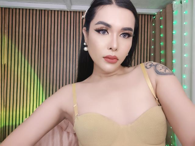 MyLuvNavi has long black hair, wearing a yellow bra, with big tits, a nose ring, and a tattoo on her right shoulder, looking at the camera with green eyes.