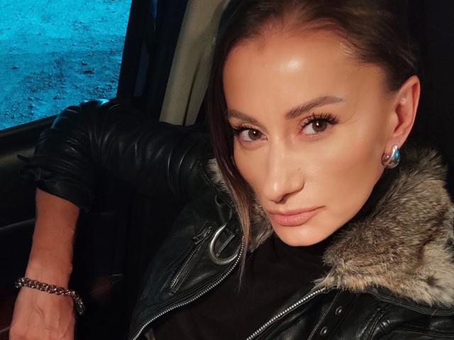 DesiredMistress-hot has a cute face, brown eyes, and a slight smirk. She's wearing a black leather jacket with a fur collar and a silver bracelet.