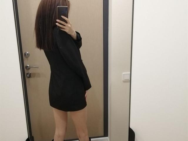 EvaRouseX with brown hair, wearing a black long-sleeve shirt, no pants, showing her bare ass, taking a mirror selfie, holding a phone, in a room.