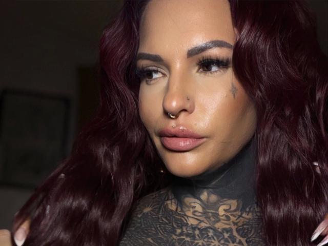 Aileenink-hot with dark red wavy hair, nose ring, tattooed neck, and full pink lips, looking to the side with glossy eyes and long lashes.