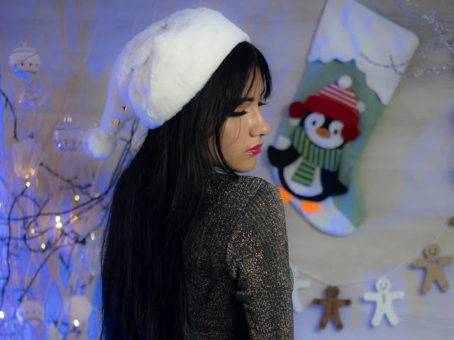 LizzeJoy with long black hair, wearing a white fluffy hat and a sparkly gray sweater, has her eyes closed, looking cute with a small, cute penguin sock in the background.