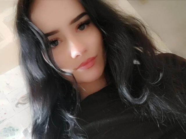 NinaLecker-hot has long black hair, full eyebrows, and pink lipstick. She's wearing a black shirt, with a soft, slightly smiling face and blue eyes.