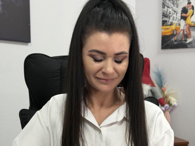 Viollia with long black hair in a high ponytail, wearing a white shirt, has closed eyes and a subtle smile, showing her cute, small ass and her tanned skin.
