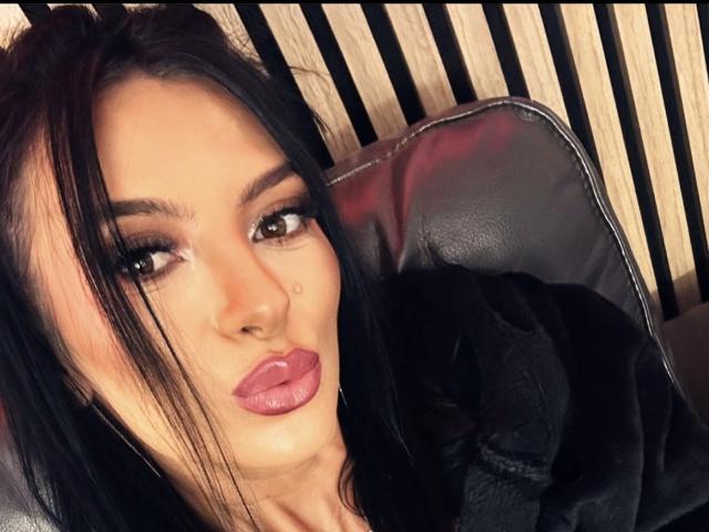 KinkyAmelie hat schwarzes Haar, braune Augen und volle, rosafarbene Lippen, mit denen sie eine schmollende Miene macht. Sie trägt ein schwarzes Oberteil und hat einen kleinen Schönheitsfleck auf ihrer rechten Wange..