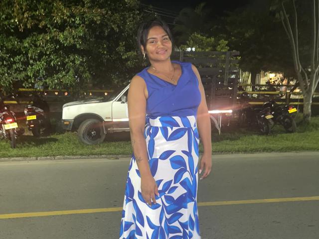 SusanaDiaz, with medium tits and a smile, wears a blue sleeveless top and white skirt with blue leaf patterns, standing on a nighttime road.