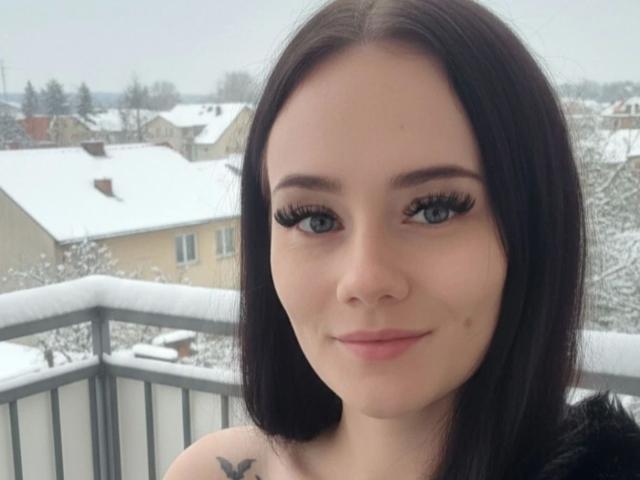 NinaLecker-hot has pale skin, dark brown hair, blue eyes, long black eyelashes, small nose, pink lips, subtle smile, and a small butterfly tattoo on her left shoulder.