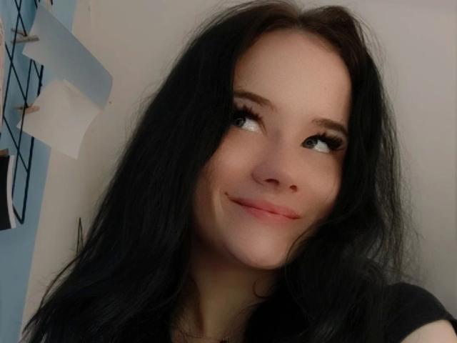 NinaLecker-hot with long black hair, looking up with a small smile, has cute eyes and a slightly pouty face, wearing a black shirt, and showing her tits.