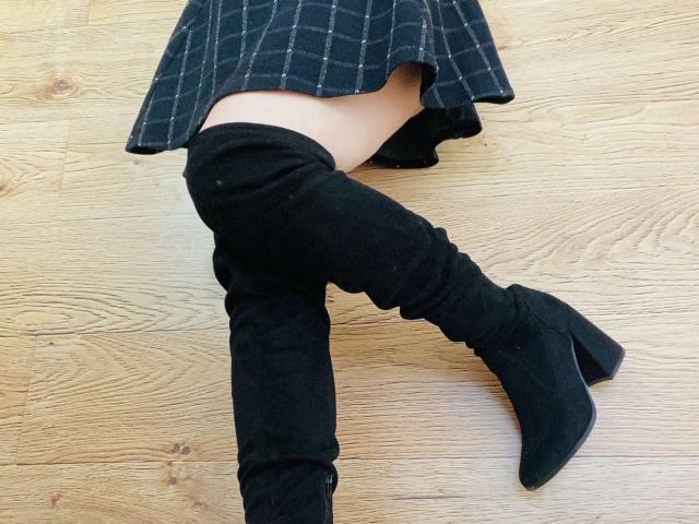 KarKutie's black thigh-high boots and plaid skirt, showing her pale skin and a bit of her ass, on a wooden floor. Boots have chunky heels.