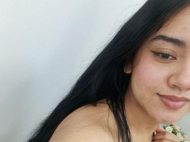 SalomeLee tem cabelos longos e pretos, pele clara e um sorriso discreto. Ela está mostrando seu rosto com seios pequenos e olhos castanhos, vestindo uma blusa sem alças..