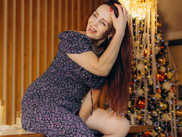 AlexisLovelyy with long red hair, wearing a floral dress, smiling, hand in hair, showing off her tits, standing on a table, crystal chandelier in background, sexy.