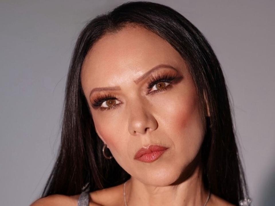 Cleoember8 hat dunkelbraune Augen, langes schwarzes Haar und macht ein schmollendes Gesicht. Sie trägt dezentes Make-up mit orangefarbenem Lippenstift und hat einen hellen Hautton..