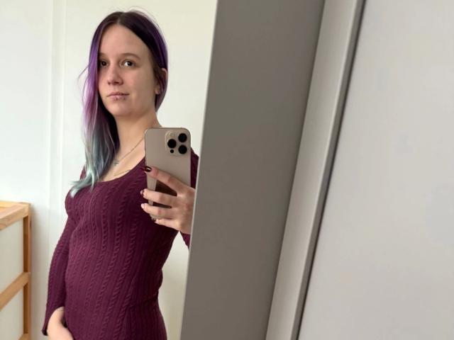 Sophiesoreal77-hot with purple-blue gradient hair, wearing a maroon knitted dress, holding a gold iPhone, taking a mirror selfie, showing a subtle smile and small breasts.