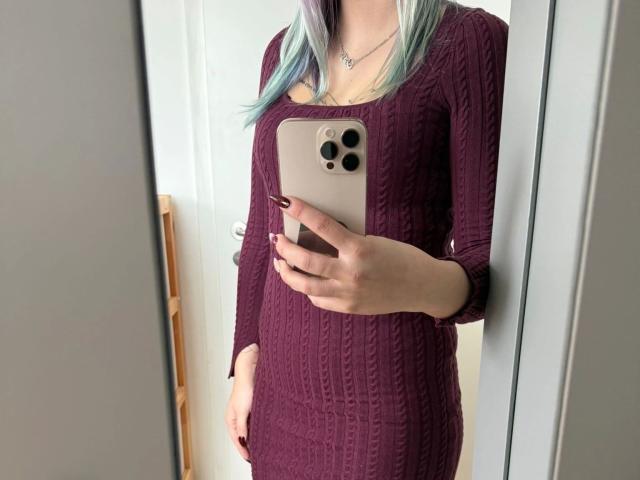 Sophiesoreal77-hot with pale skin, wearing a tight purple rib-knit dress, holding a gold iPhone, showing her tits and ass in a mirror selfie.