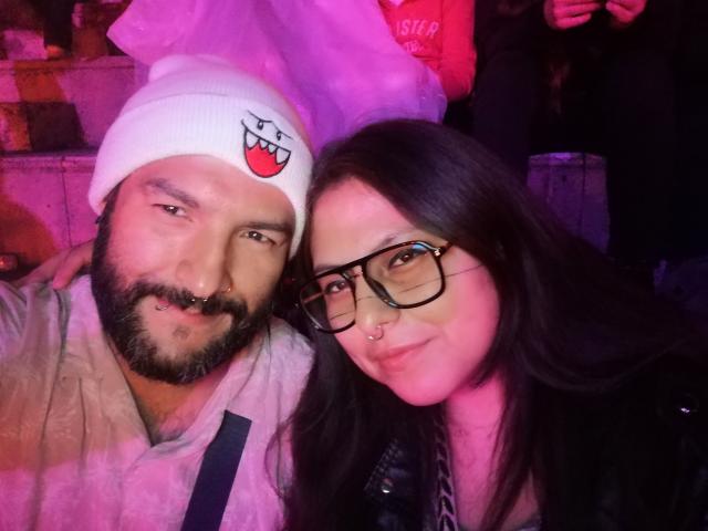 SektethLilith with a beard and white hat featuring a vampire face, and SektethLilith with glasses and nose ring, smiling together. SektethLilith on the left, SektethLilith on the right.