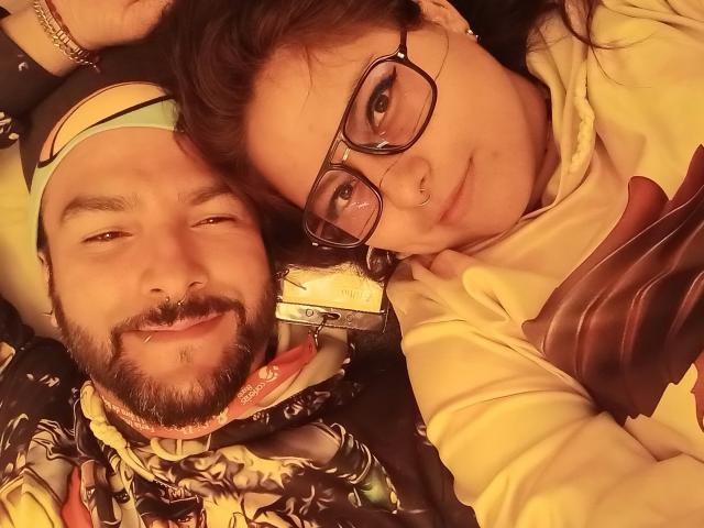 SektethLilith and SektethLilith, a dude with a beard and a nose ring, and a chick with glasses and a nose ring, lying down, smiling at the camera.