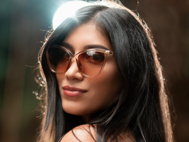 MaraClara with long black hair, brown skin, and brown sunglasses, looking over shoulder with subtle smile, glossy pink lips, soft light in hair. Boobs not visible, ass not visible.