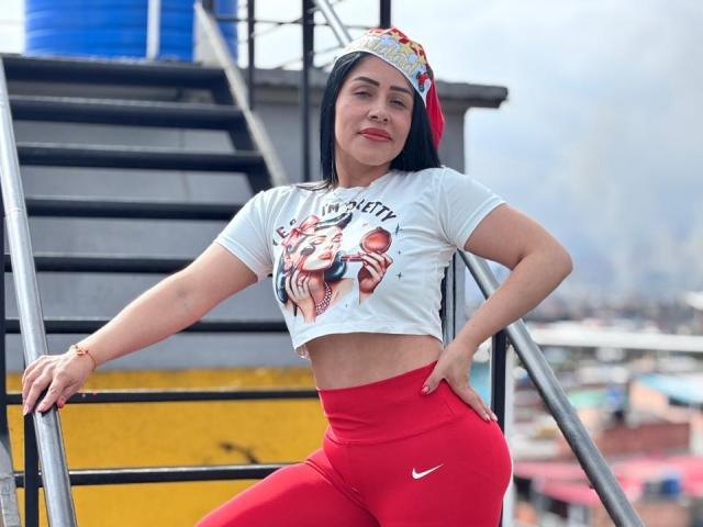 KinkyVane with dark hair, red Nike pants, white crop top, and colorful headband, leaning on stairs, smiling, showing a flat, toned stomach and small, firm ass.