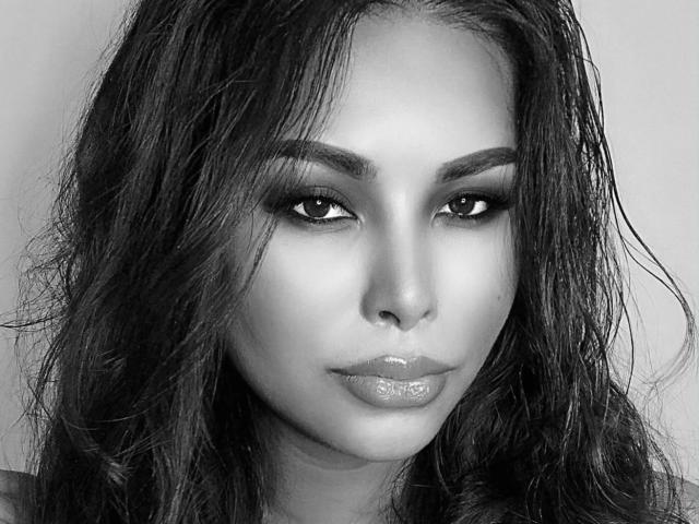 TsLexie-hot has glossy lips, wet wavy hair, and sultry eyes. Her eyebrows are thick and she's staring directly at the camera. Black and white photo.
