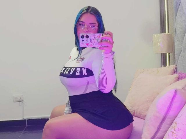 AuroraSantorini with blue hair, glasses, and a mask, taking a mirror selfie. She's wearing a white long-sleeve top and black skirt, showing her big boobs and curvy ass.