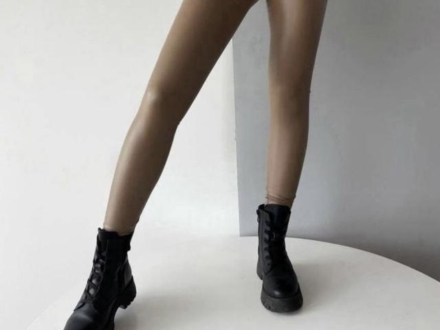 GlariyaHot's legs in black leather lace-up boots, standing on a white surface, showing off her toned, tan-skinned thighs. Her boots have a slight heel and rugged soles.