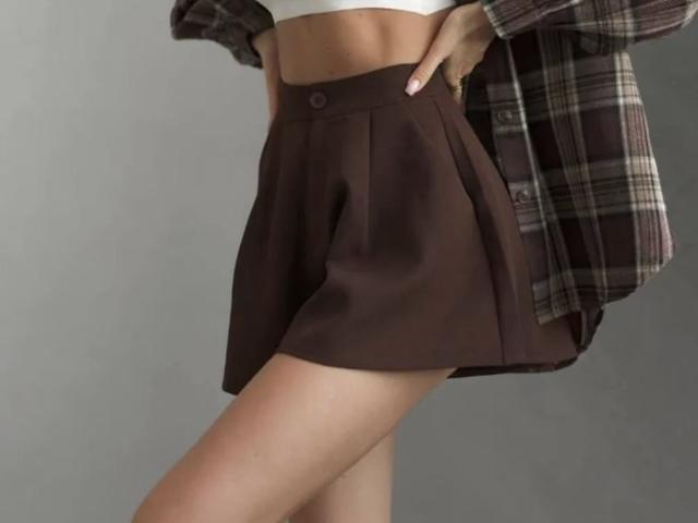 GlariyaHot's brown pleat skirt, showing her bare ass, with a white crop top and brown plaid shirt hanging off her shoulder. Her hand rests on her hip.
