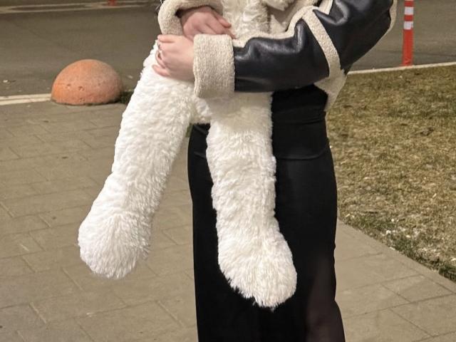 GlariyaHot's fluffy white bunny ears, hanging from her black dress and black leather sleeves, with her hands holding them. She's wearing a beige, fur-trimmed jacket.