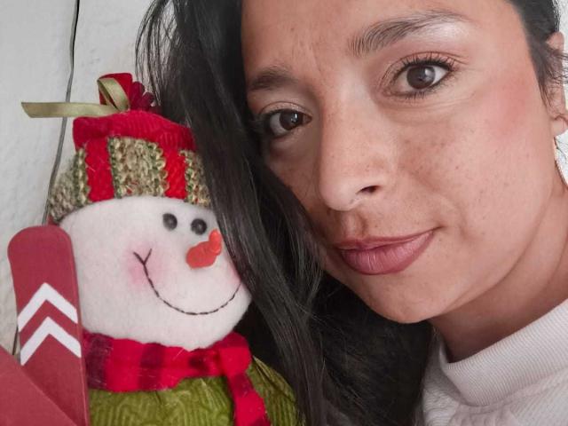 StangelarRivera's face with dark hair, red lipstick, and earrings, next to a cute, red-nosed, white, woolen snowman with a green scarf and red hat, holding red skis.
