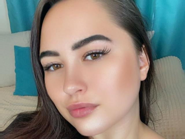 BossyLady has brown eyes, long dark brown hair, thick eyebrows, and full pink lips. Her face is slightly tanned with a smooth, shiny complexion. She looks directly at the camera.