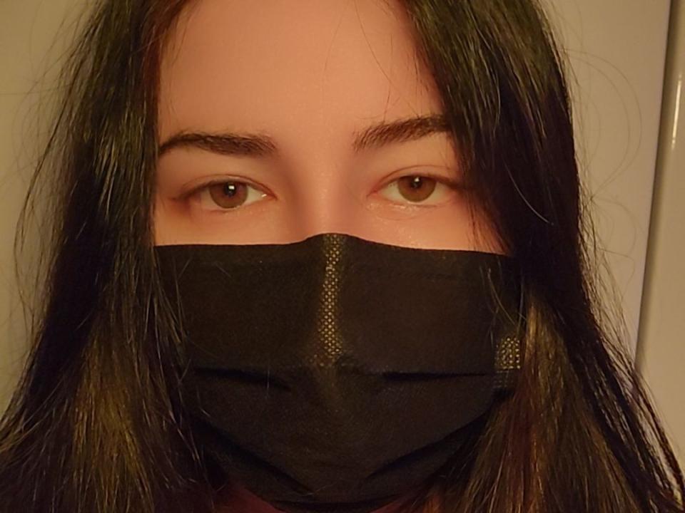 Lanarei with brown eyes, black mask covering nose and mouth, long dark brown hair, and slightly raised eyebrows. Sheer black fabric visible over her mouth.