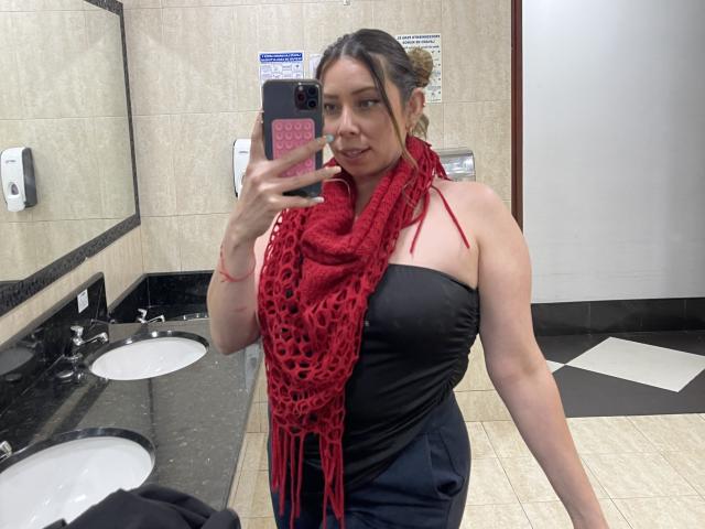 JennyLawry with red knit scarf, black strapless top, and black pants, taking a mirror selfie in a bathroom, showing her medium tits and smiling.