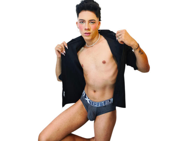 BlakeNoir, shirtless, wearing gray underwear with "HARLEY" on the waistband, black open shirt, necklace, short dark hair, tattoos on right wrist, white background, standing, slightly kneeling.