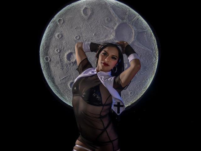 MiaBellucci in a sheer black top, exposing her tits, arms raised, wearing a nun's headdress, against a giant moon. Black background, moon centered. Sheer, sexy, and seductive.