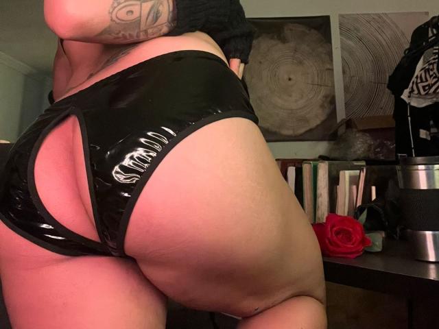 SteffanyTaylor's shiny black latex butt cheeks are prominently displayed, with a cut-out revealing her pink, plump ass. She has a tattoo on her left arm.