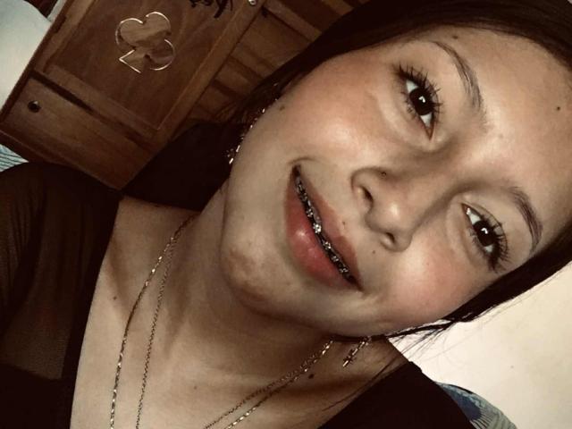 ValenPerdomo has a cute smile with metal braces on her teeth, brown eyes, and black hair. She's wearing a black top and a gold necklace.
