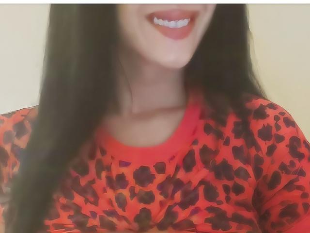 Kannelldesirs with long black hair, smiling with red lipstick, wearing a red leopard print shirt, showing her collarbone and upper chest. Boobs not visible, focus on her face.