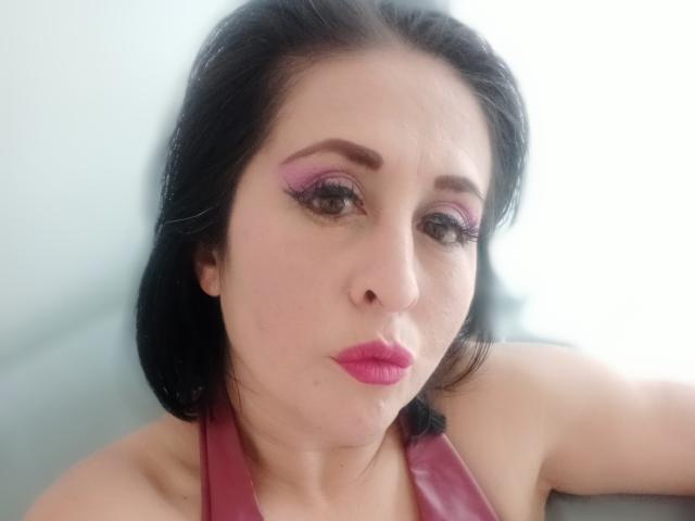 ScarletMilfX with pink eyeshadow, black hair, pink lipstick, and a pink halter top, looking serious, showing her bare shoulders and collarbone.