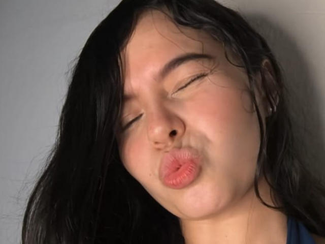 LissyCarter with closed eyes, puckered lips, and dark wet hair, making a kissing face. Her nose is slightly upturned, and she's wearing small earrings.