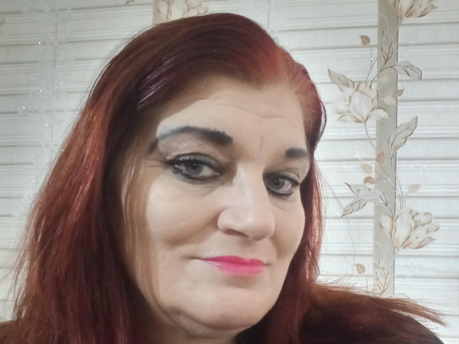 LoisBecky has red hair, black eyeliner, and pink lipstick, with a slight smile. Her ass-chin is visible, and she has a light skin tone.