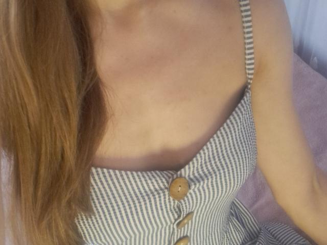 Amberia's chest, showing her small tits in a striped dress with a wooden button, and her light brown hair falling over her shoulder. Her skin is fair.