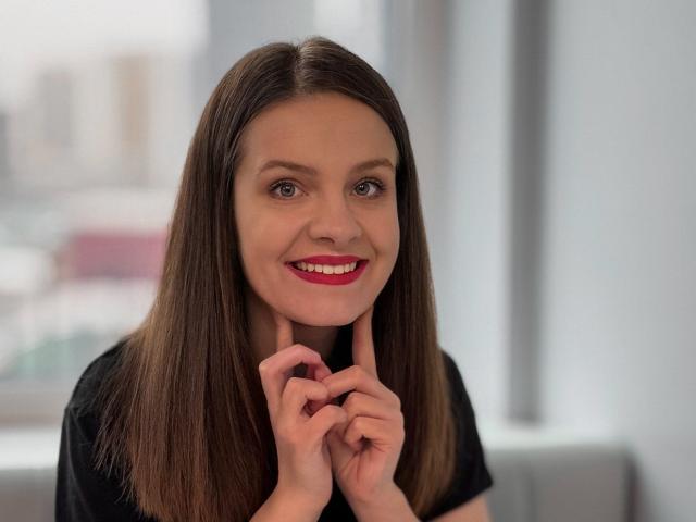 Ameliarings has straight brown hair, red lipstick, and a black shirt, with fingers near her chin, smiling softly. Her tits are average, and she's looking cute.