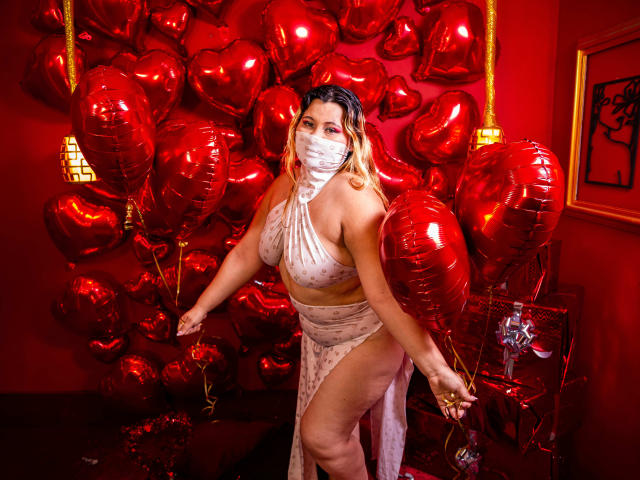 SalmaAzaman with red heart balloons, wearing a white face mask, sheer polka dot dress, showing her tits and ass, holding balloons, in a red-lit room, looking sexy.