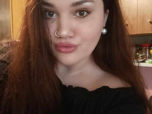 WinterPeggy has brown hair, a nose ring, and pearl earrings, wearing a black top with pink lipstick, and looking at the camera with a slight smile.