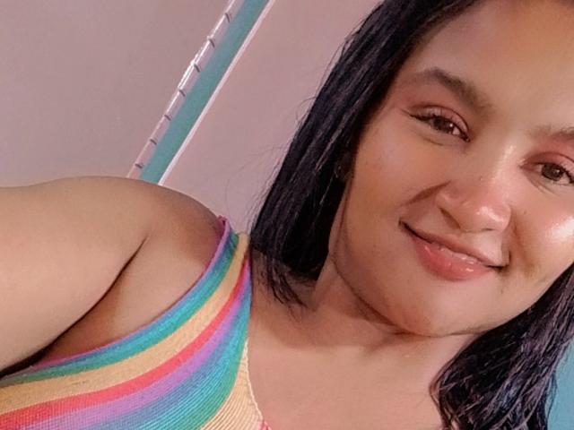 SusanaDiaz with medium tits, smiling, wearing a rainbow-striped tank top, black hair, light brown skin, and subtle makeup, in a selfie.